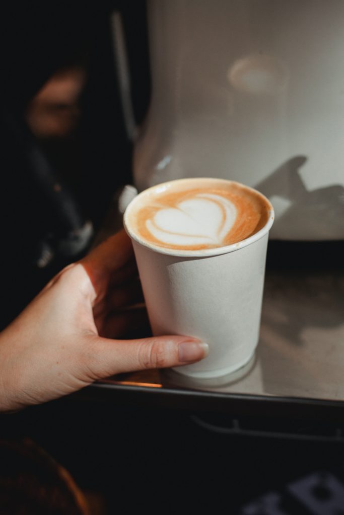 A woman reaches for a latte on a cafe table.