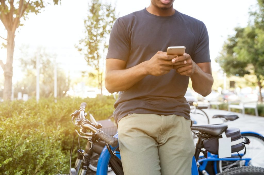 A man leaning against a bicycle makes an online purchase on his phone.
