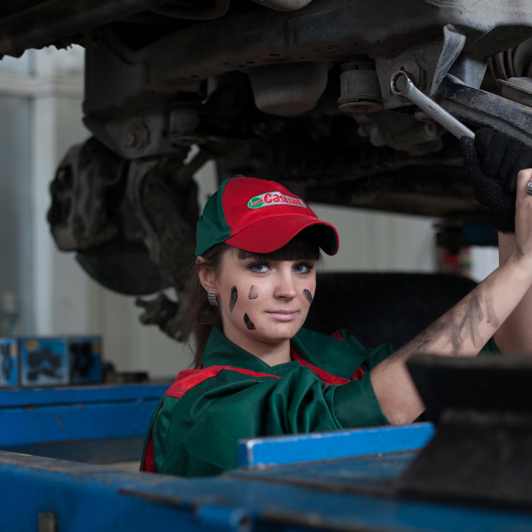 A woman holding a wrench beneath a car