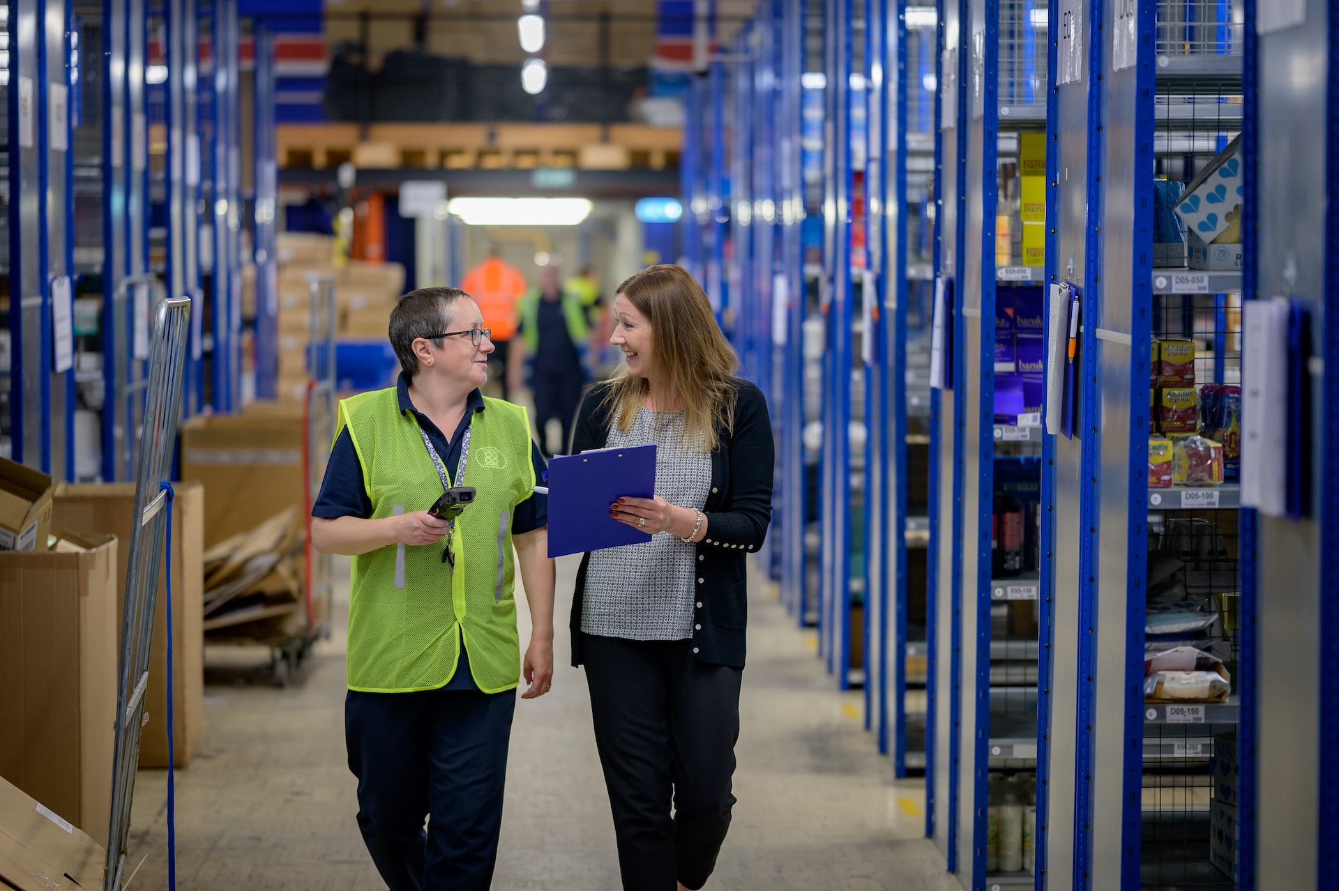 Two women walking by inventory in a warehouse